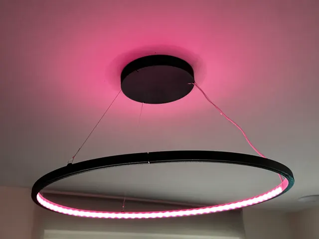 A black ring pendant lamp glowing pink under a white ceiling
